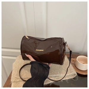 Détail d'un sac baril en cuir verni marron foncé avec logo doré et bandoulière fine