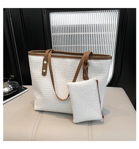 Detailed view of white woven tote bag with matching small pouch on a beige leather bench