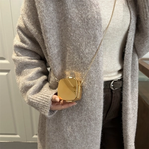 Mini gold mirror-finish square box bag with elegant chain strap on a knit sweater