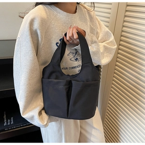 Detail of a black nylon tote bag with dual front pockets held in a stylish setting