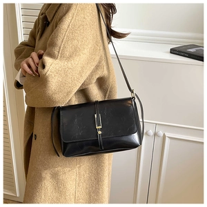 Détail d'un sac bandoulière en cuir noir avec barre métallique et fermoir rond