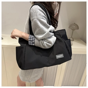 Dettaglio di una grande borsa tote nera con tasca laterale e scritta 'FASHION' moda