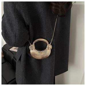 Dettaglio della borsa a mezzaluna dorata con texture in rilievo su cappotto scuro