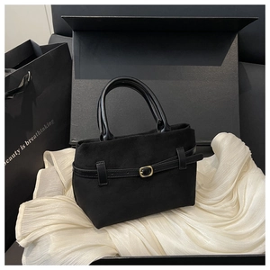 Gros plan d'un sac seau en daim noir avec sangle en cuir et boucle dorée dans un coffret
