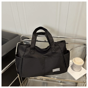 Dettaglio della borsa tote in nylon nero con tasche anteriori ed etichetta FASHION bianca