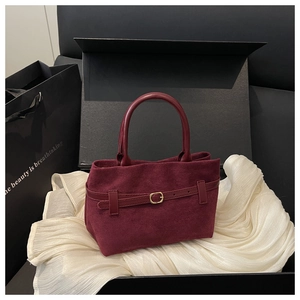 Détail d'un sac à main bordeaux en daim mat avec boucle dorée et texture de la poignée