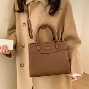 Brown faux leather tote bag with top handles and strap on camel wool coat model