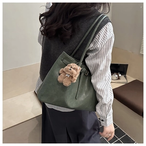 Détail du sac cabas en cuir vert foncé avec breloque ours en peluche et boucle en métal