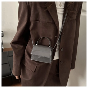 Close-up of a mini grey patent leather crossbody bag styled on a brown blazer outfit