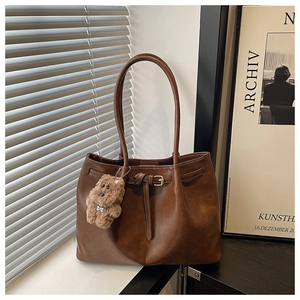 Detail of a dark brown retro tote bag with a plush bear charm on a windowsill