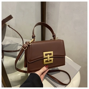Detail of dark brown leather crossbody bag featuring a geometric gold metal clasp and mirror