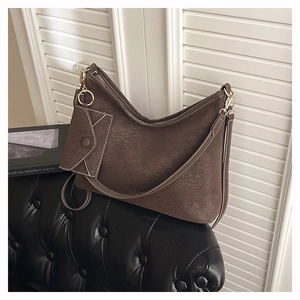 Close-up of coffee brown suede hobo bag with a matching small pouch on a black sofa
