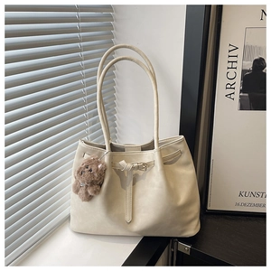 Close-up of beige tote bag with smooth texture, leather strap detail and plush bear charm