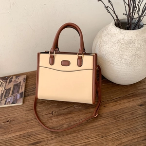 Détail d'un sac cabas beige avec des anses en cuir marron sur une surface en bois rustique