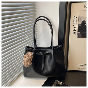 Detail of black leather tote bag with belt buckle straps and brown plush bear charm