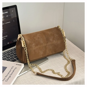 Detail van donkerbruine suède crossbody tas met kruissteek en gouden ketting