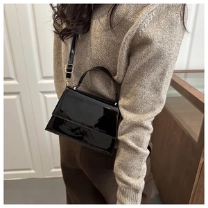 Detail of black patent leather crossbody bag with gold hardware on a mannequin