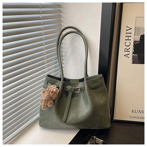 Macro shot of dark green matte tote bag featuring belt buckle detail and plush bear charm