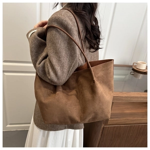 Detail view of large brown faux suede tote bag worn over the shoulder in a cozy room