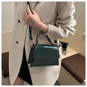 Close-up of green patent leather crossbody bag with gold hardware worn on beige wool coat
