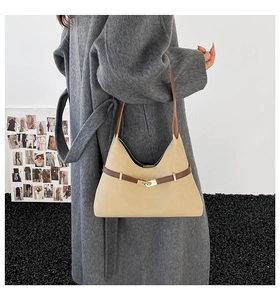 Close-up of beige suede shoulder bag with brown strap and gold metal buckle on a model