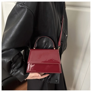 Detail of dark red patent leather square handbag worn with a black leather jacket