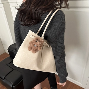 Grand sac cabas beige en similicuir avec pendentif ours porté sur un pull en maille grise