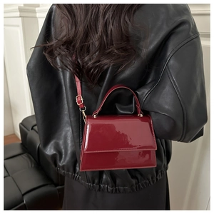 Deep red patent leather crossbody bag with a glossy finish and golden metal buckle details