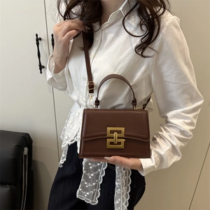 Brown leather crossbody bag with gold buckle on a stylish model in casual outfit