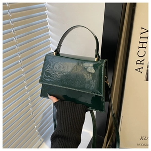 Detail view of a dark green patent leather handbag with gold metal hardware and top handle
