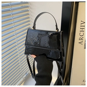 Detail of glossy black patent leather handbag with gold hardware and curved handle