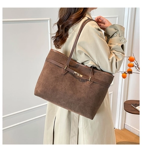 Detail of a large brown suede tote bag with gold buckle on a model in a trench coat