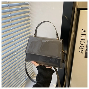 Detail of dark grey patent leather handbag with glossy finish and gold metal hardware