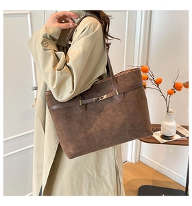 Detail of a large brown suede tote bag featuring a metallic buckle and premium texture