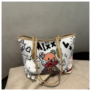 Detail of white canvas tote bag with graffiti art, brown leather straps, and cloud charm