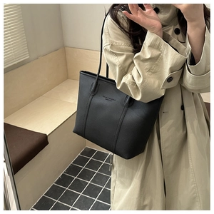 Close-up of black pebble grain leather tote bag with embossed logo on beige trench coat