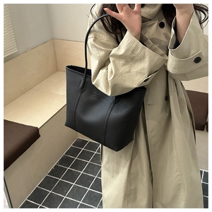 Detail view of black pebble leather tote bag shown on a model with elegant beige coat