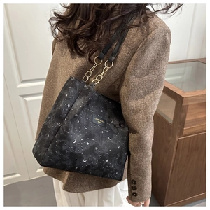 Detailed view of black tote bag with star moon print and gold chain strap on model
