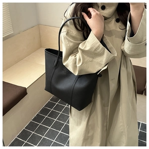 Detail of large black pebbled leather tote bag worn with beige trench coat for commute