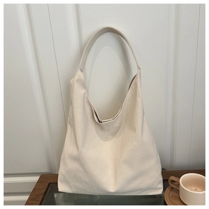 Detail view of a creamy white minimalist hobo tote bag placed on a modern glass tabletop