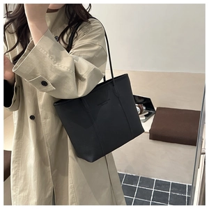 Detail of black pebbled leather tote bag featuring thin straps and embossed logo design