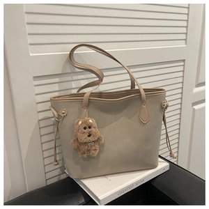 Detailed view of beige suede tote bag with brown edge piping and plush bear pendant