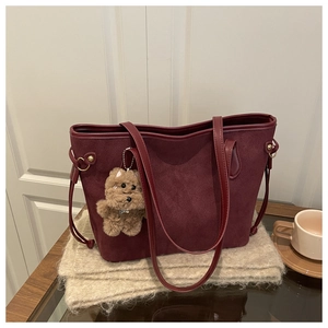 Detailed close-up of dark red suede tote bag with brown plush bear charm and side drawstrings