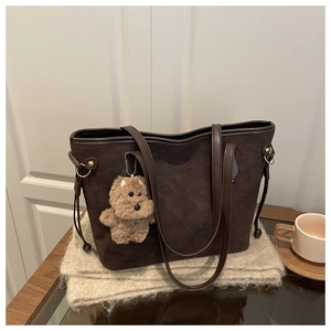 Detail of a brown suede tote bag with a cute plush bear pendant on a cozy winter scarf