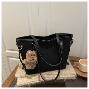 Detail of a black canvas tote bag featuring a cute brown poodle plush charm on the handle