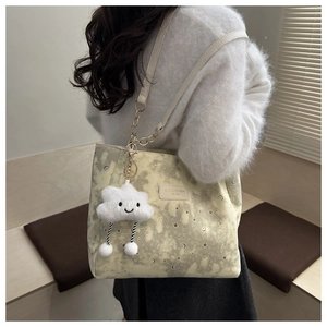 Detail of beige tote bag with star patterns, gold chain strap, and plush cloud charm