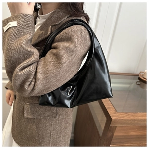 Black crescent hobo bag in glossy patent leather worn with a vintage brown blazer