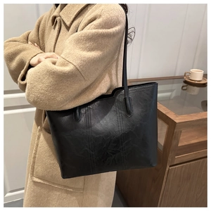 Detail of a black leather tote bag with vertical stitching shown on a beige wool coat