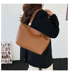 Side view of a brown oil wax leather tote bag worn by a model against a white wall
