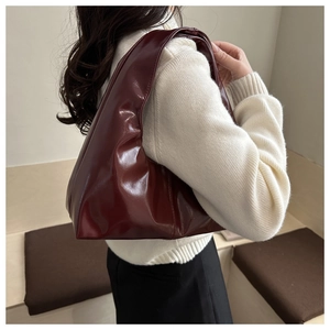 Detail of dark burgundy hobo bag in glossy leather worn by a model in a minimalist setting